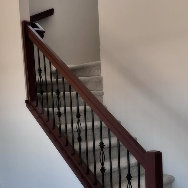 Stained wood handrail with decorative black balusters installed by Nand Finishing