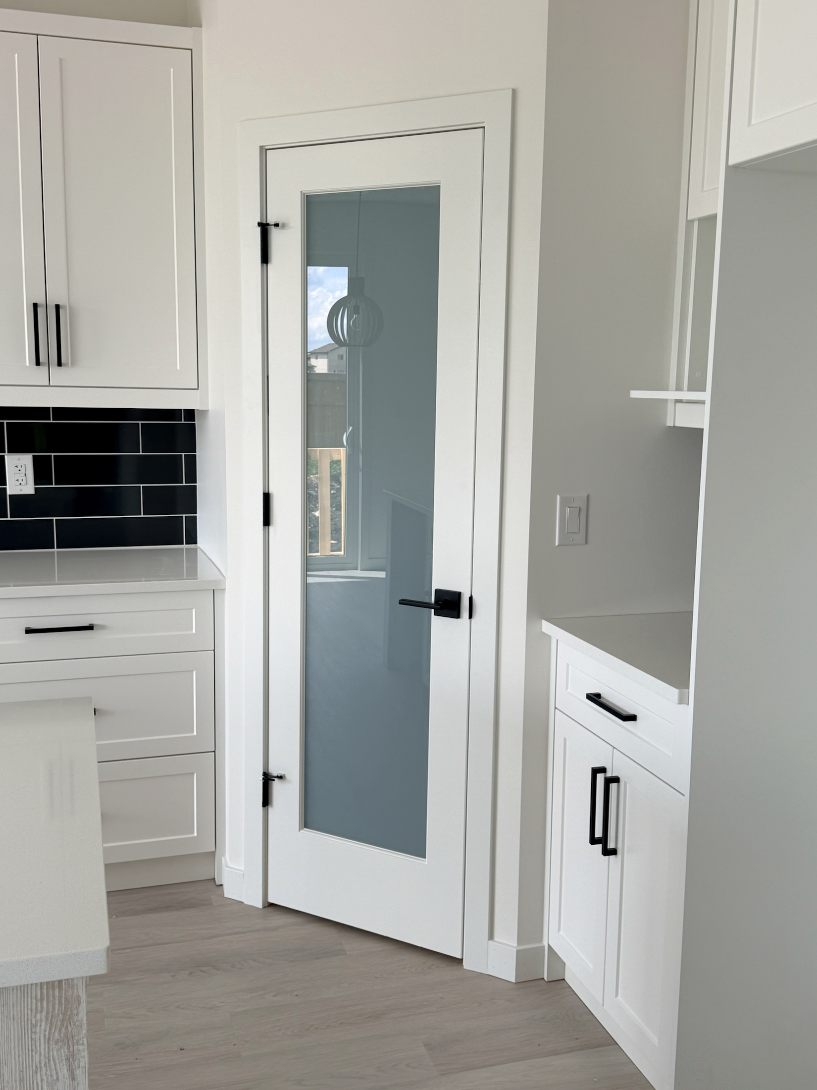 White cabinetry, black hardware, backsplash, and finished door casing