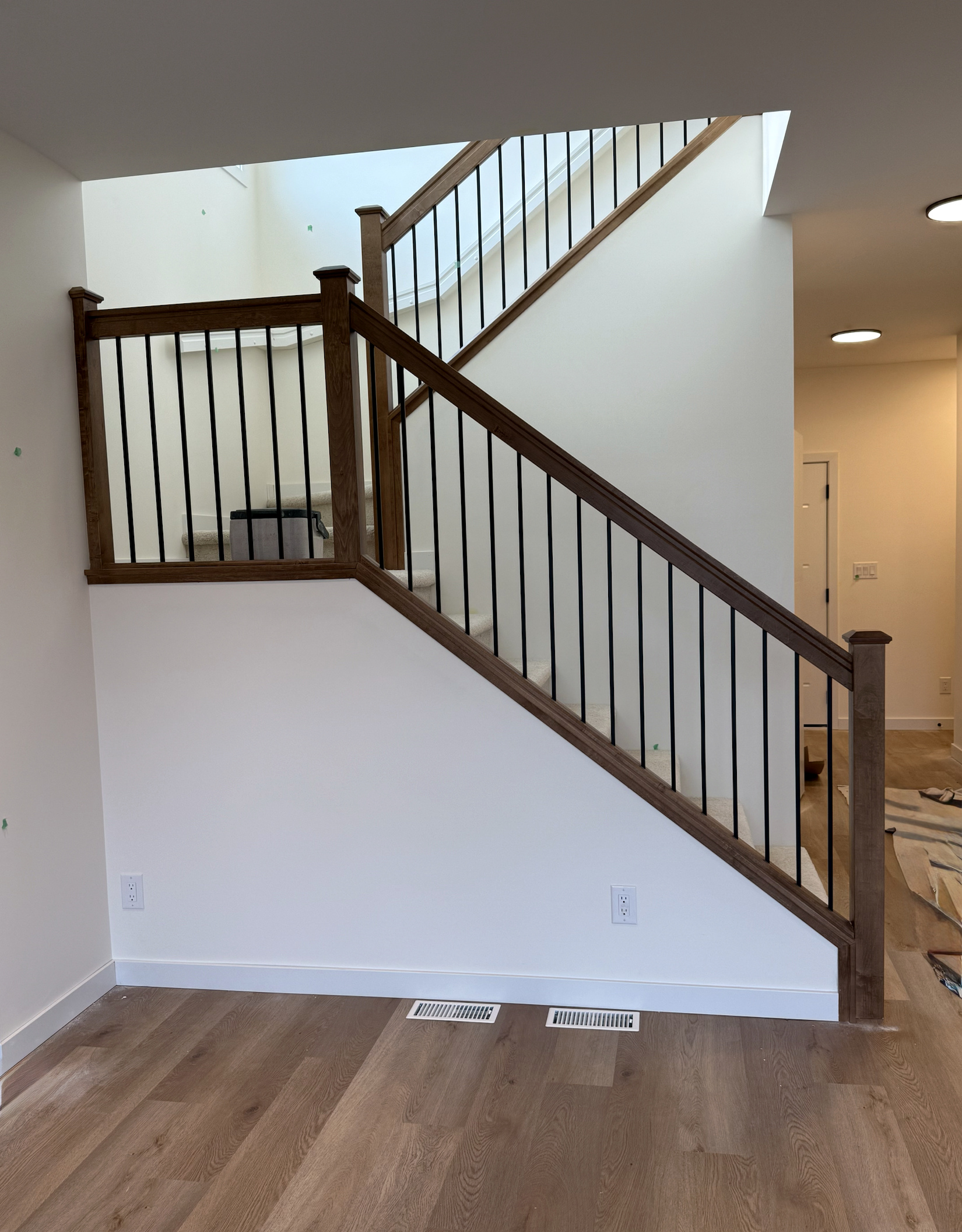 Stained wood stair railing with black metal balusters installed by Nand Finishing