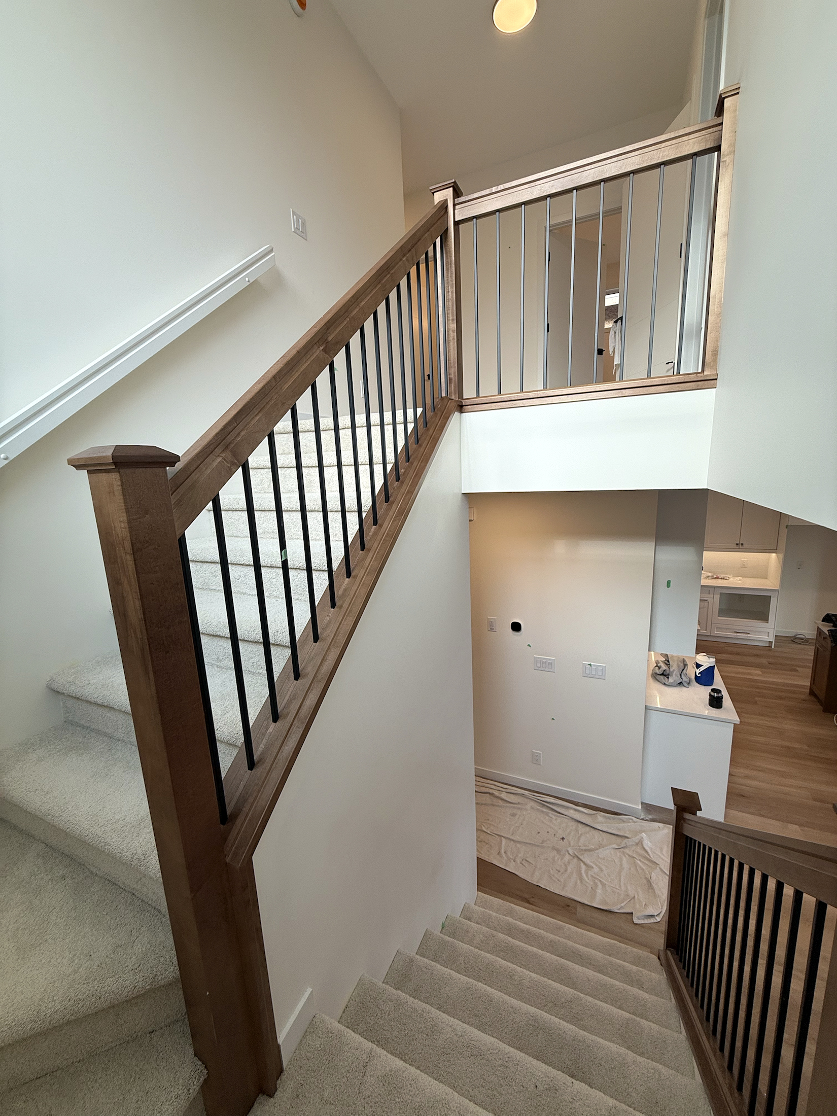 Full-height stained wood staircase with black balusters and matching upper guardrail
