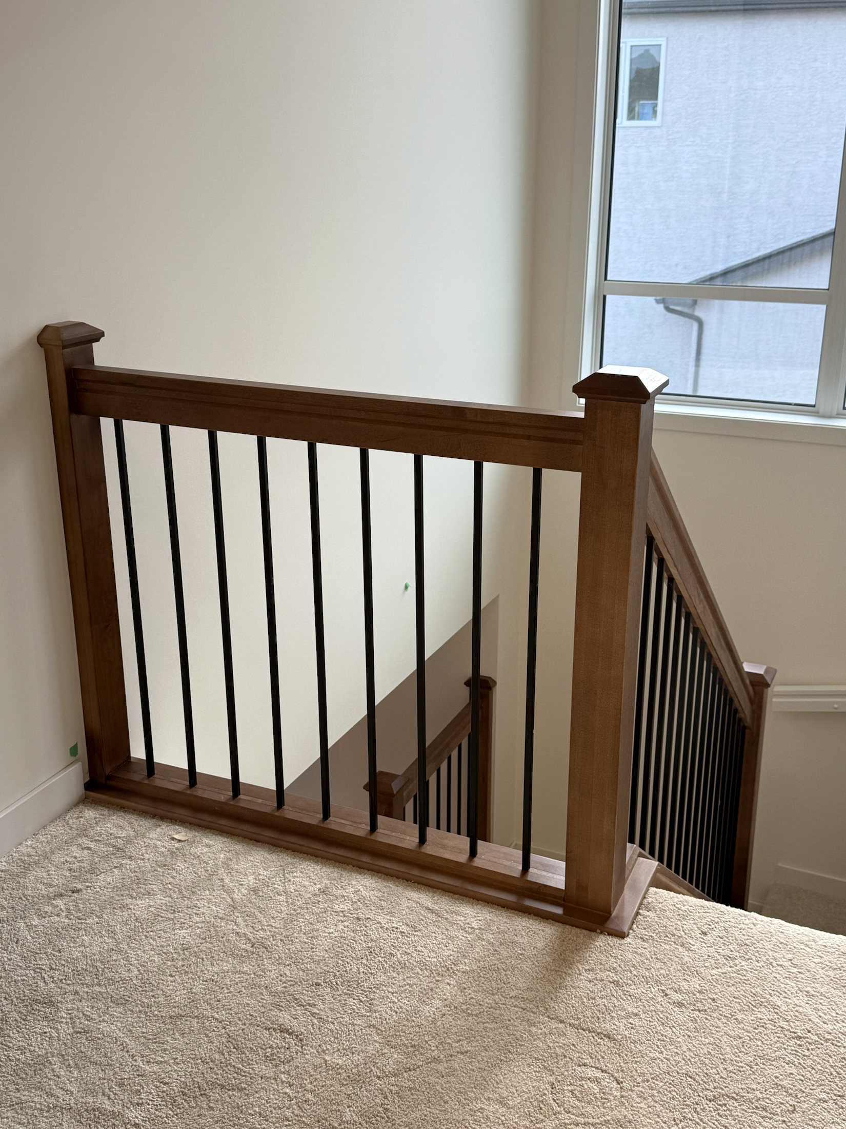 Stained wood upper landing guardrail with black metal balusters